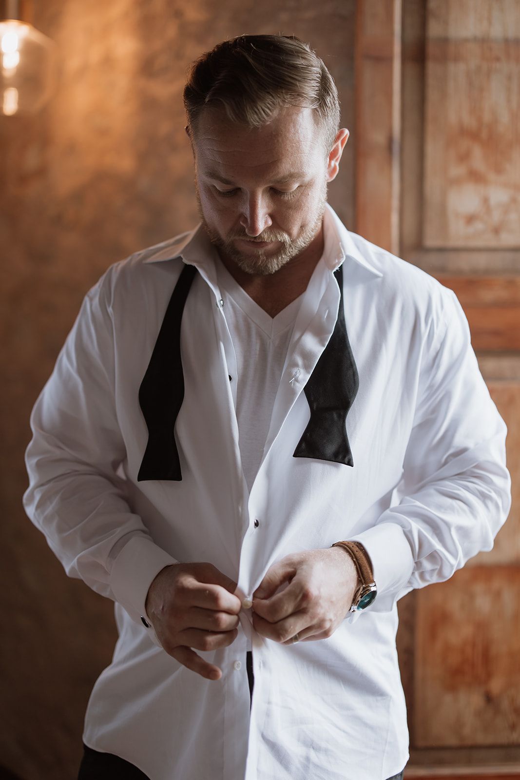 Person adjusting black bow tie while wearing crisp white formal shirt.