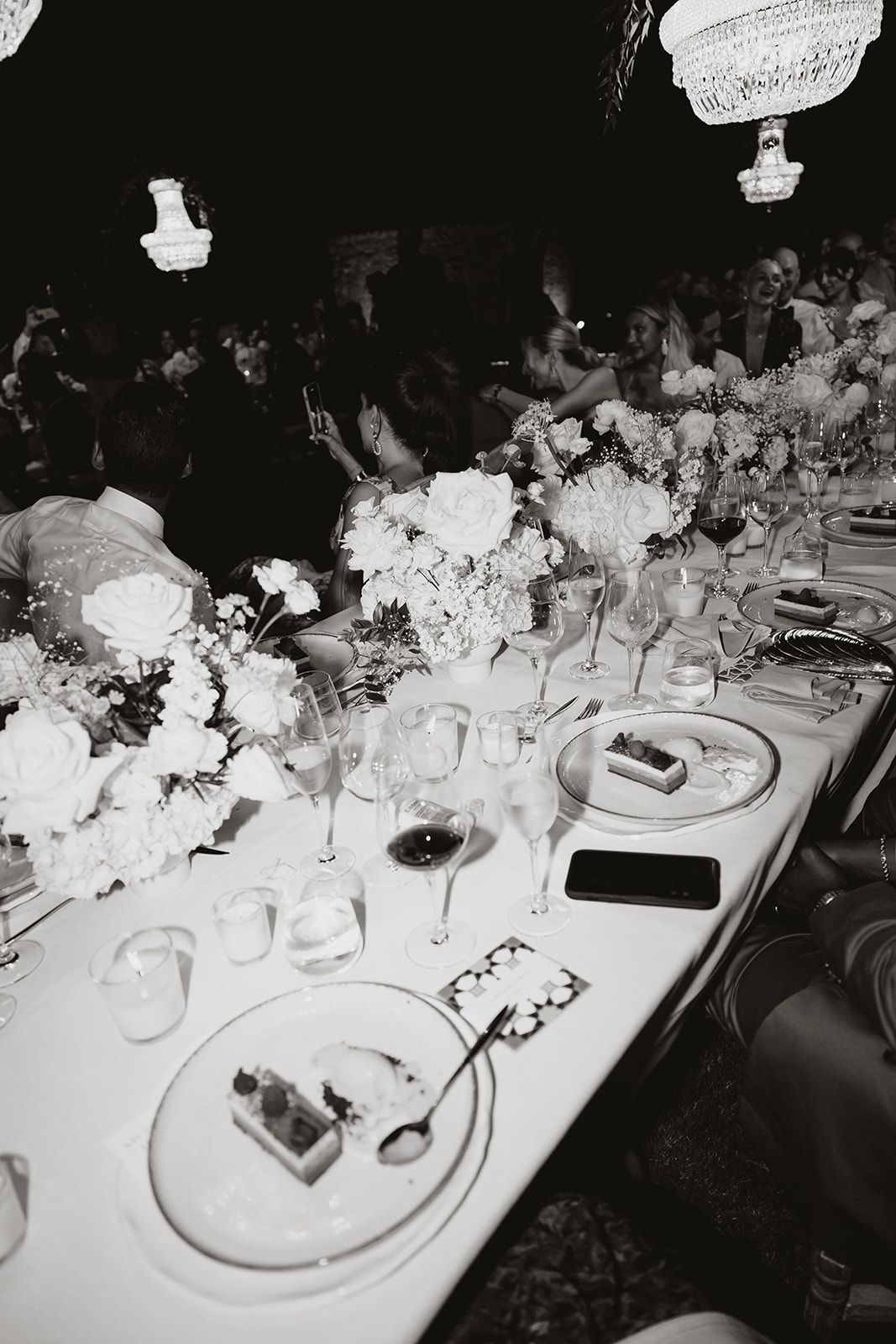Elegant wedding reception table setting with crystal chandeliers and white floral centerpieces.