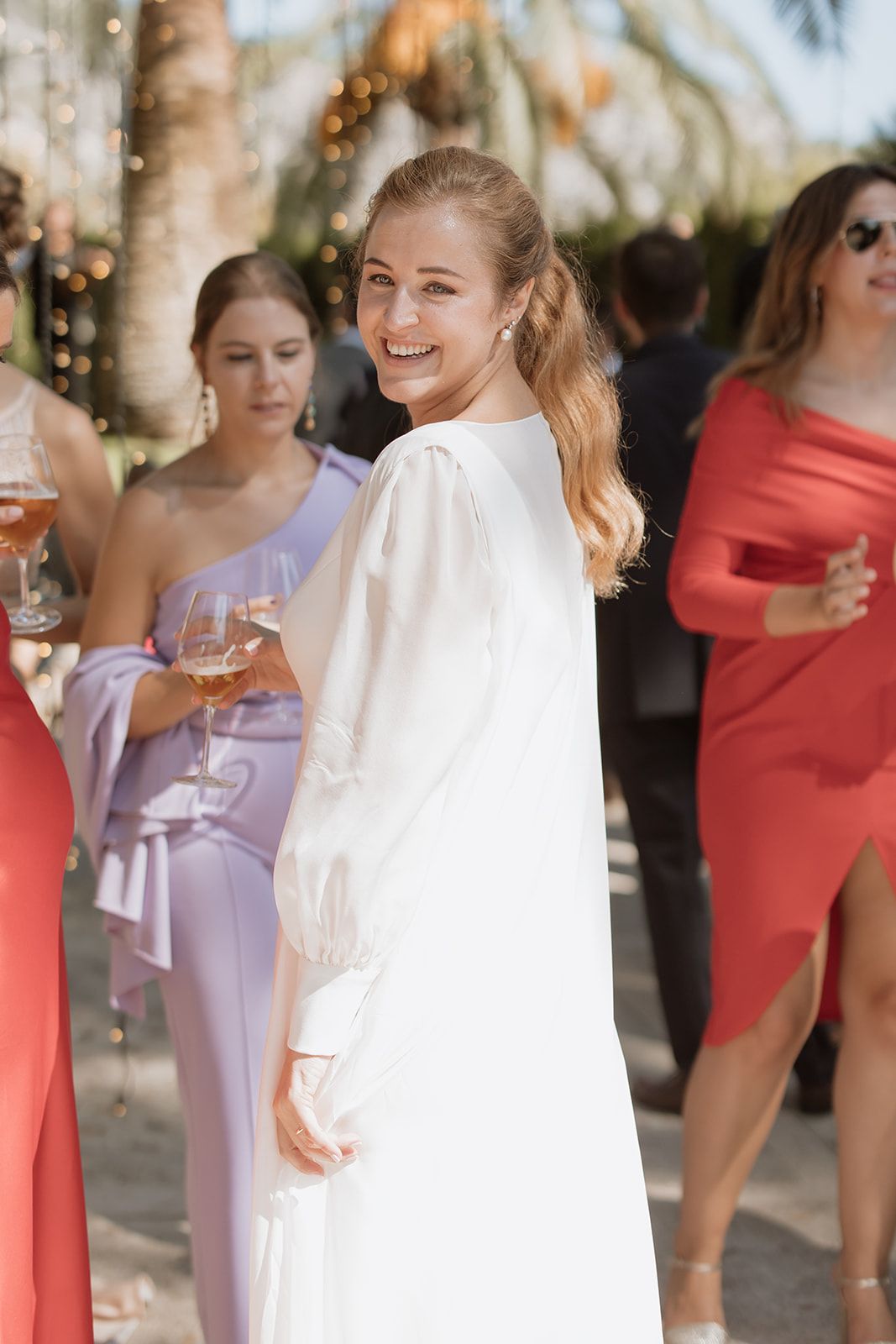 Wedding party members in colorful dresses enjoying drinks at outdoor celebration.