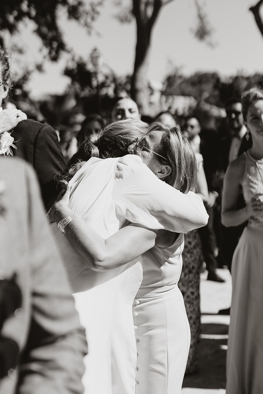 Wedding couple embraces intimately during outdoor celebration surrounded by guests.