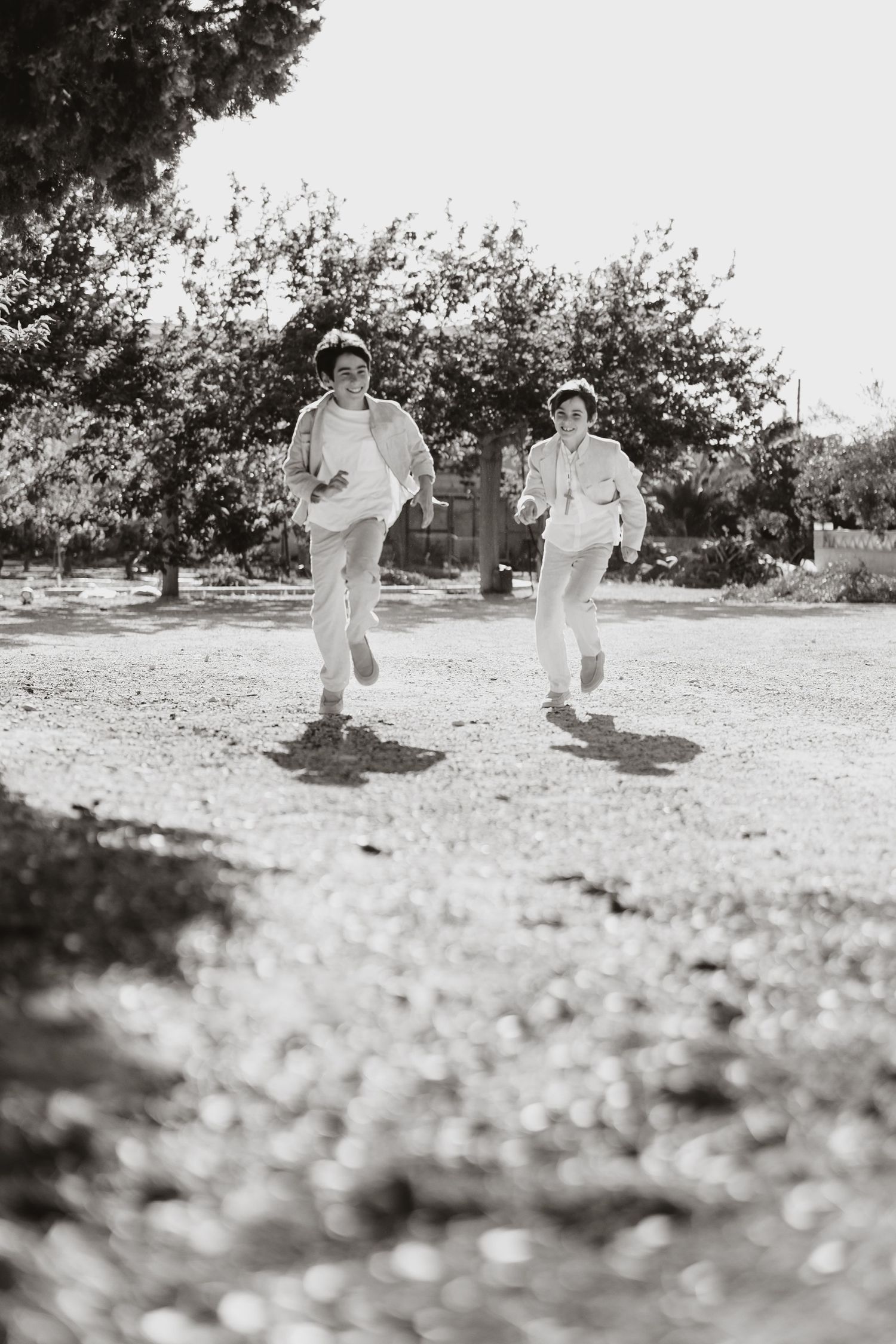 Two children in white clothes running and playing together on a dirt ground in black and white photography.