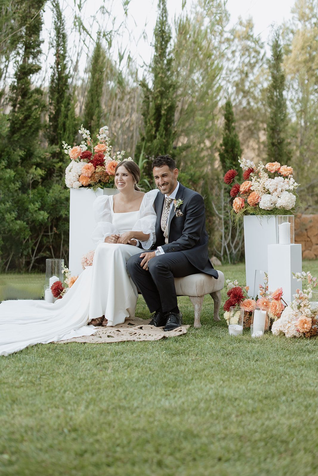 Outdoor wedding setup with elegant white pedestals adorned with coral and peach floral arrangements.