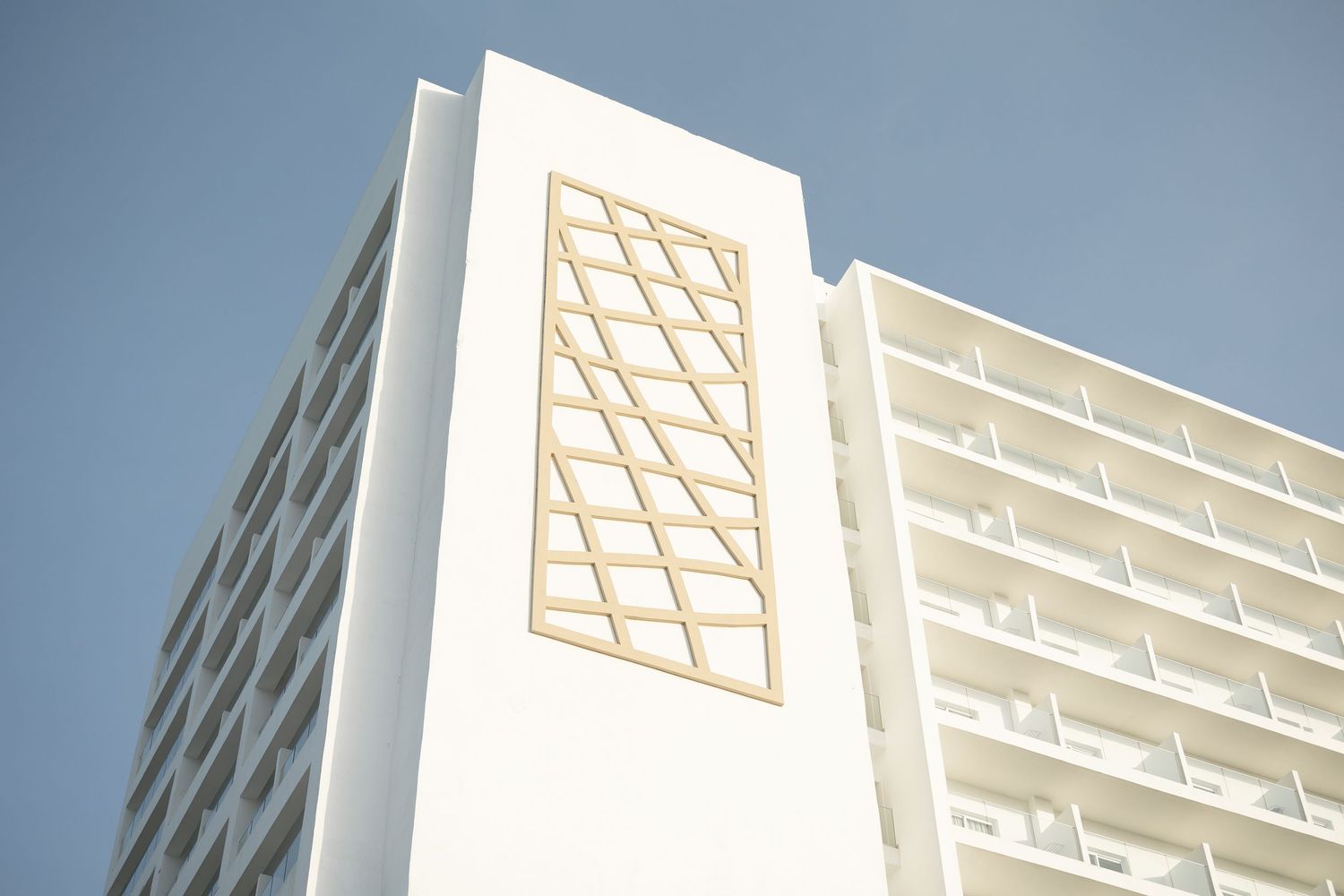 Architectural detail of white hotel facade featuring geometric pattern in warm sunlight.