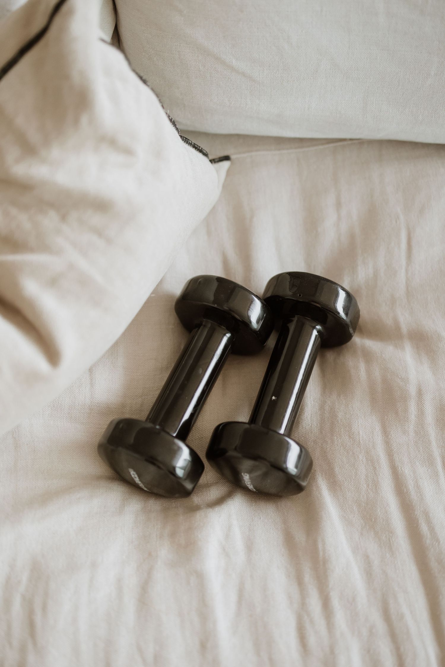 Two black dumbbells resting on white bedding.