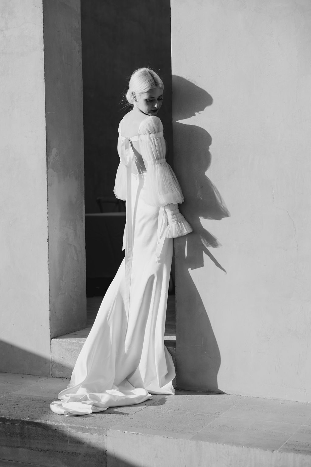 Black and white portrait of elegant gown with voluminous sleeves against architectural setting.