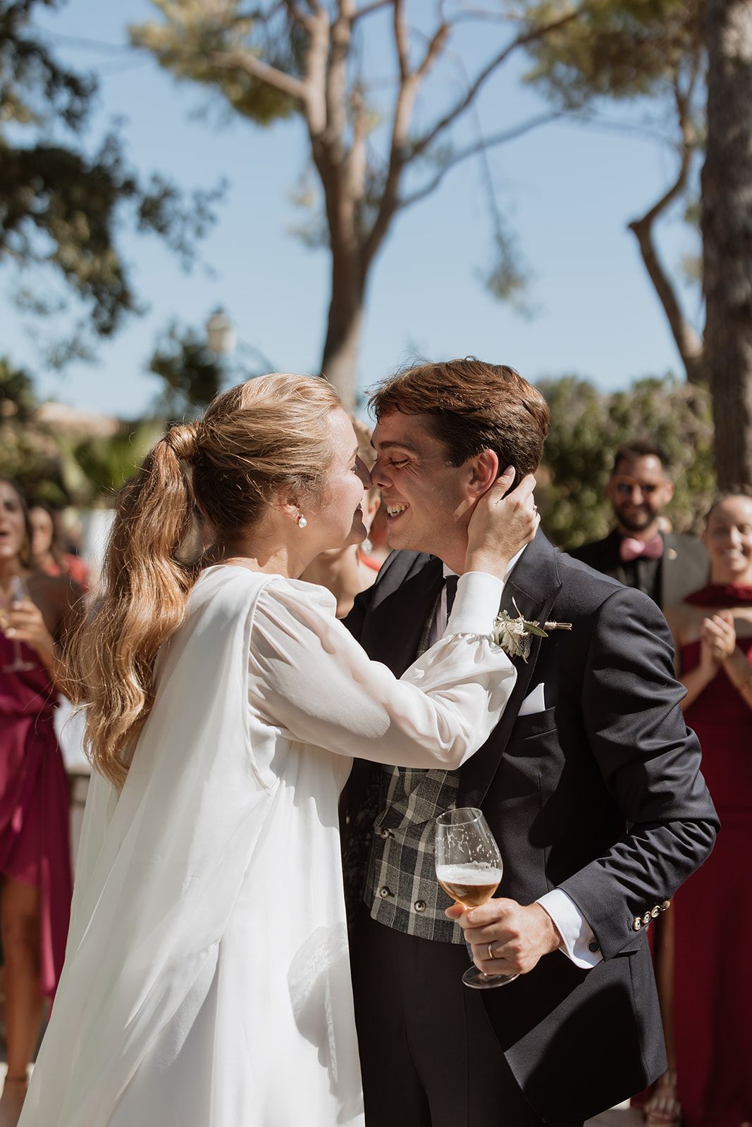 Bride and groom share romantic kiss during outdoor wedding ceremony with guests in background.