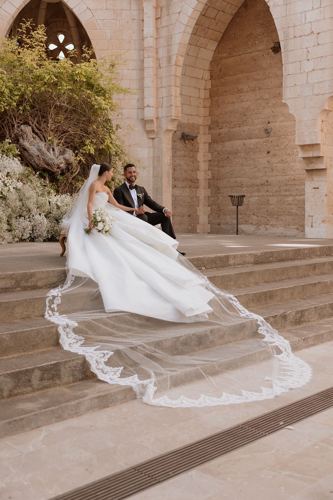 White wedding dress with long lace veil cascading down stone cathedral steps.