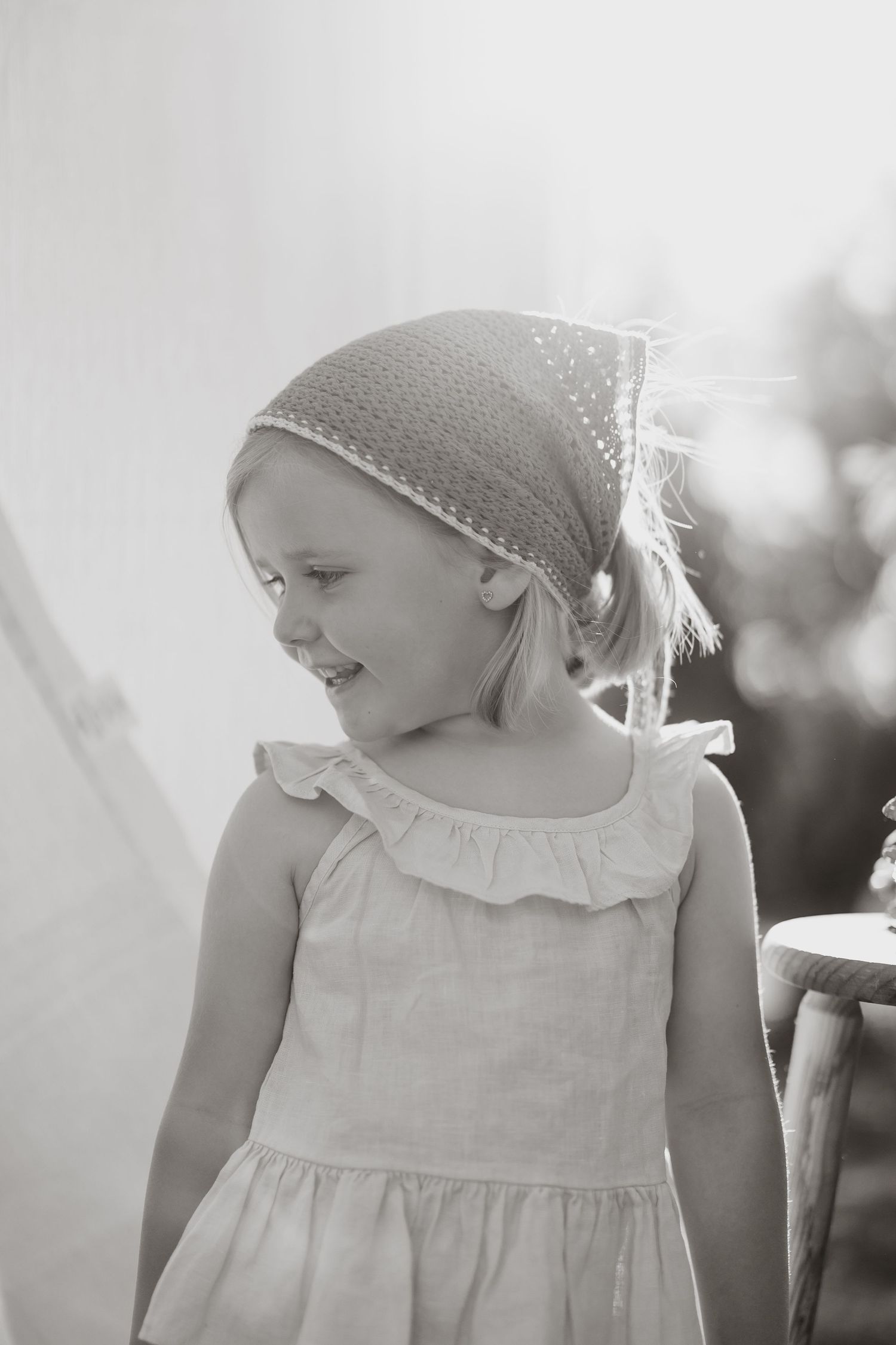 Gentle side profile portrait in white dress and knit bonnet against light background.