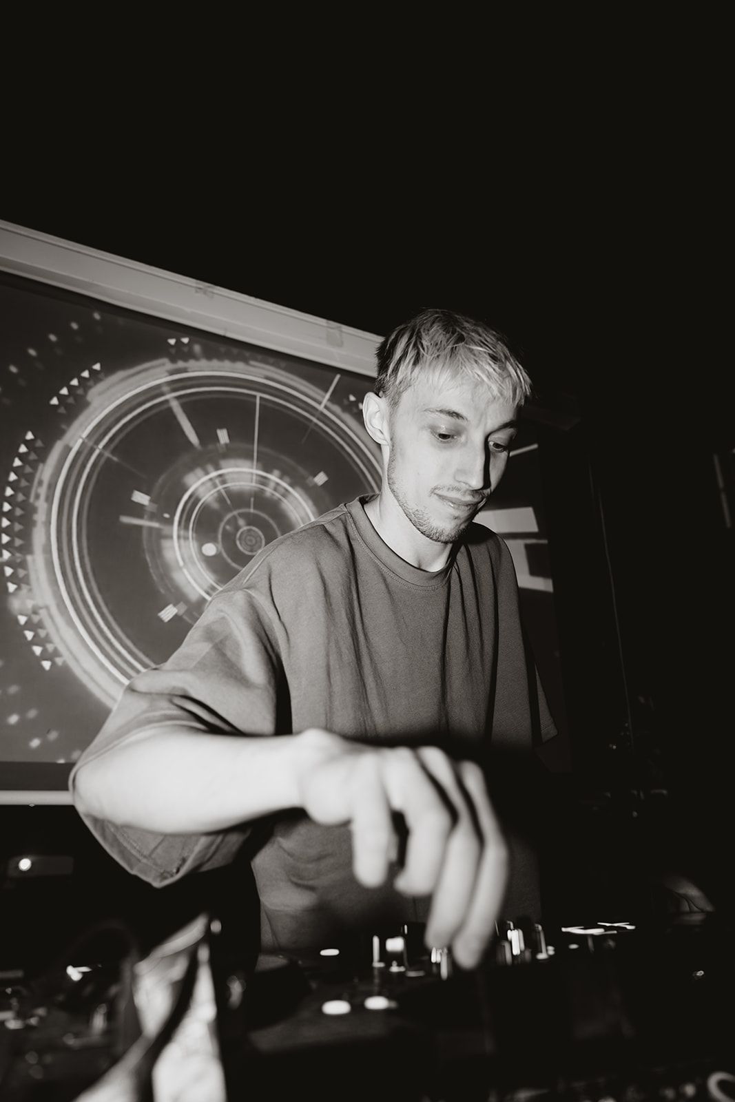 DJ performing behind decks at a nighttime event with dramatic lighting.