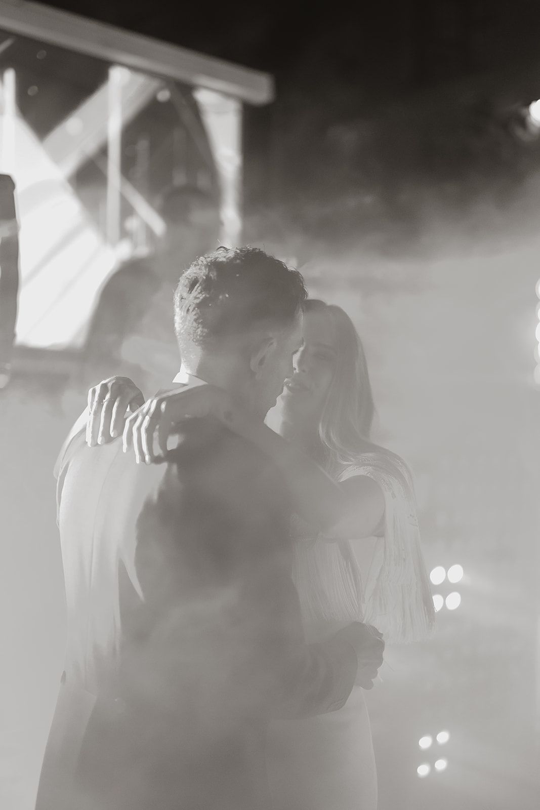 Couple sharing an intimate dance moment in atmospheric black and white lighting.