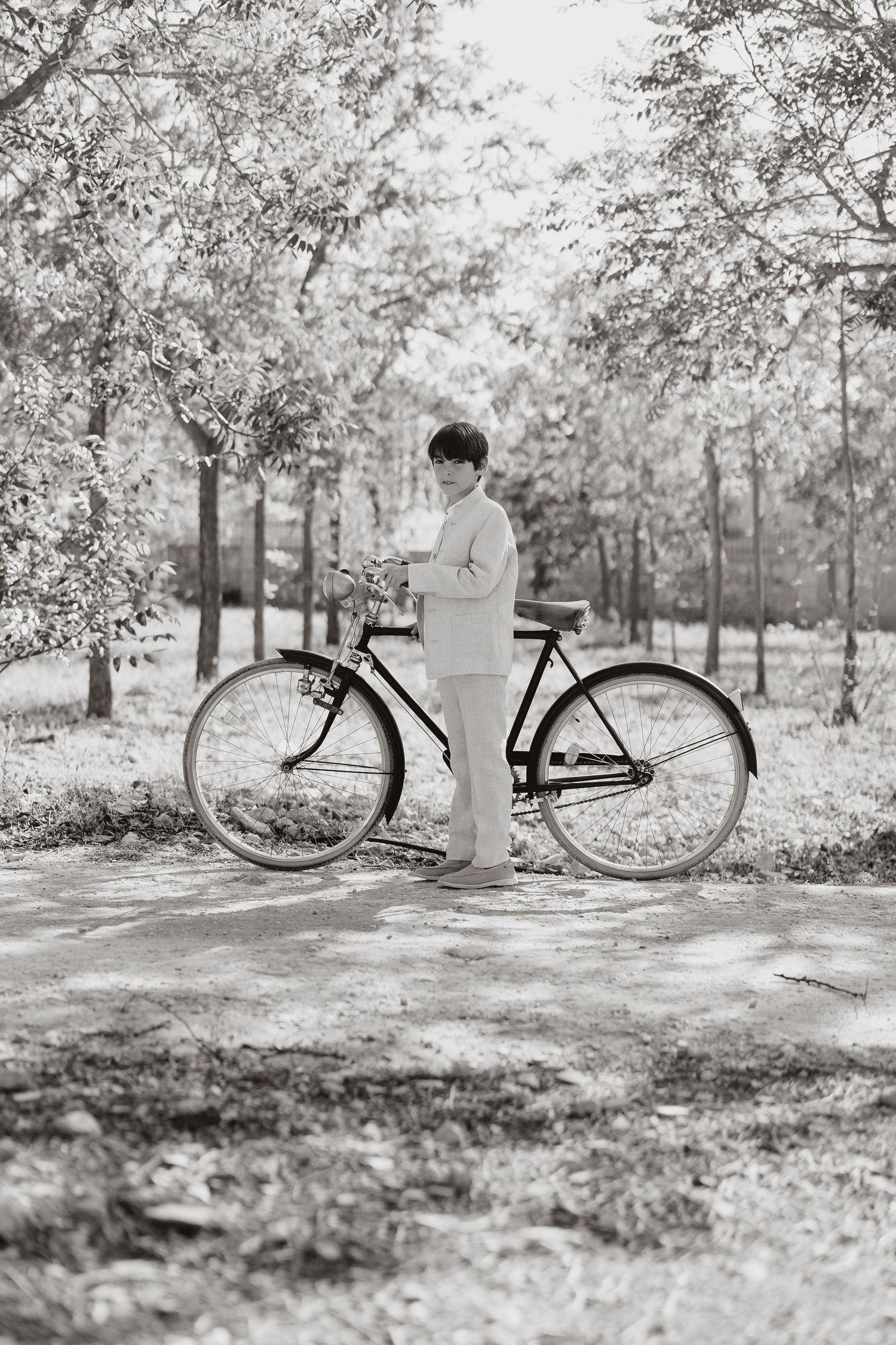 Black and white vintage photograph of a person with a bicycle standing on a tree-lined path in a park.