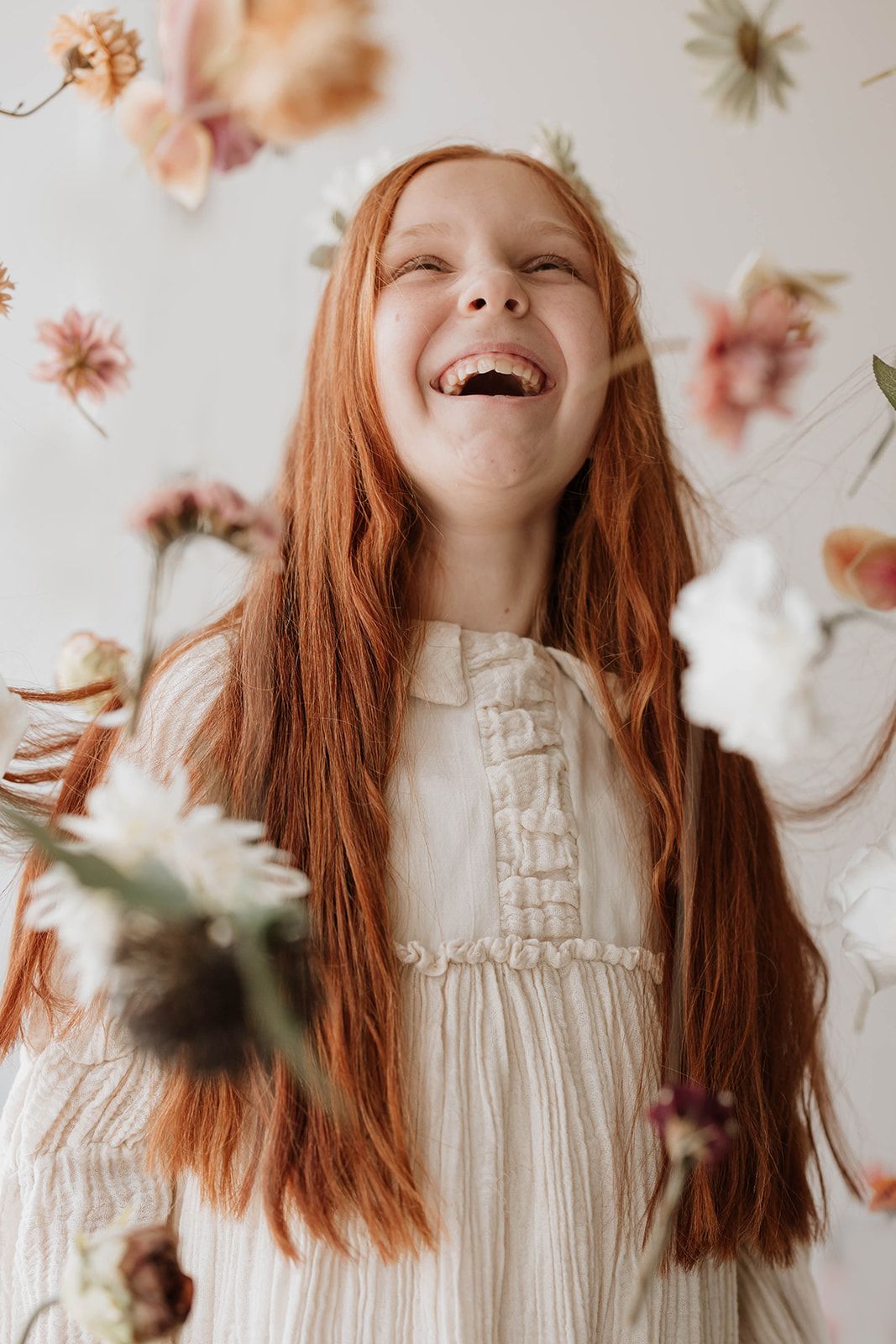 Candid laughing portrait with long ginger hair surrounded by floating botanical elements.