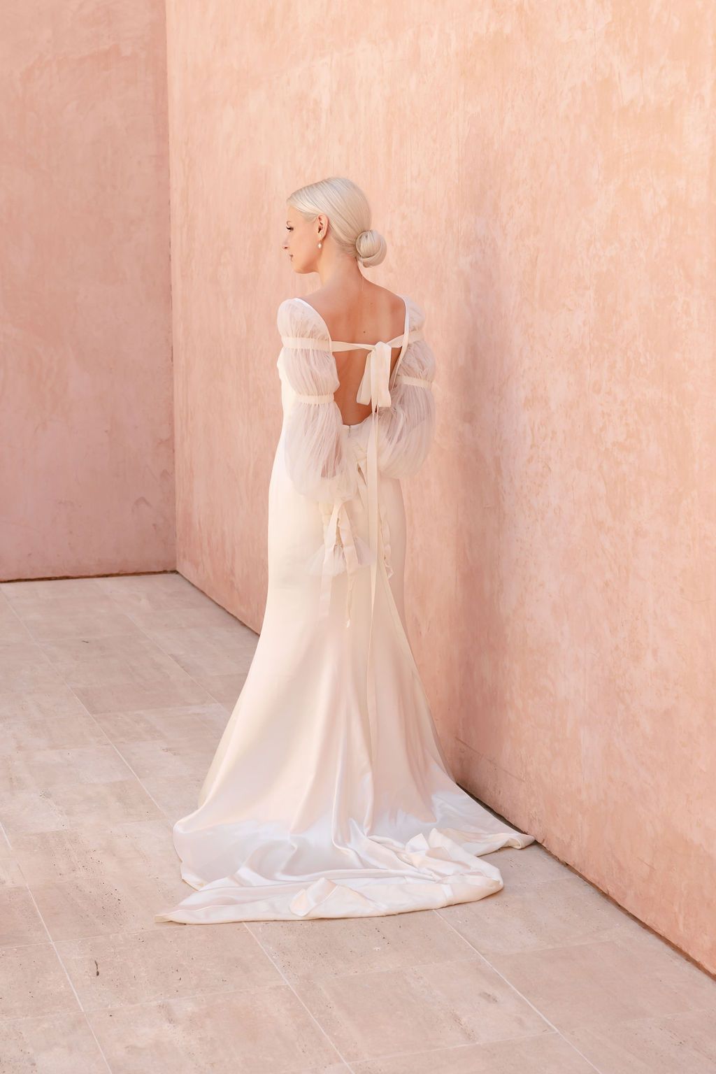 Elegant white wedding gown with train photographed against peachy pink wall.