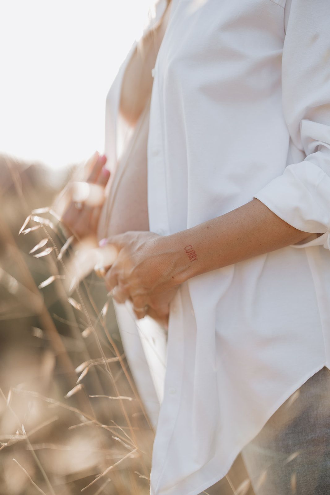 Artistic close-up of maternity pose with white shirt in golden sunlight.