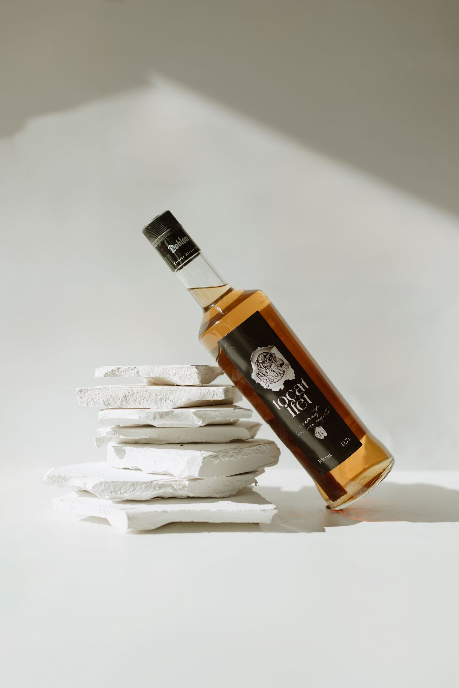 A bottle of spirits leaning on stacked white coasters creating an artistic composition.