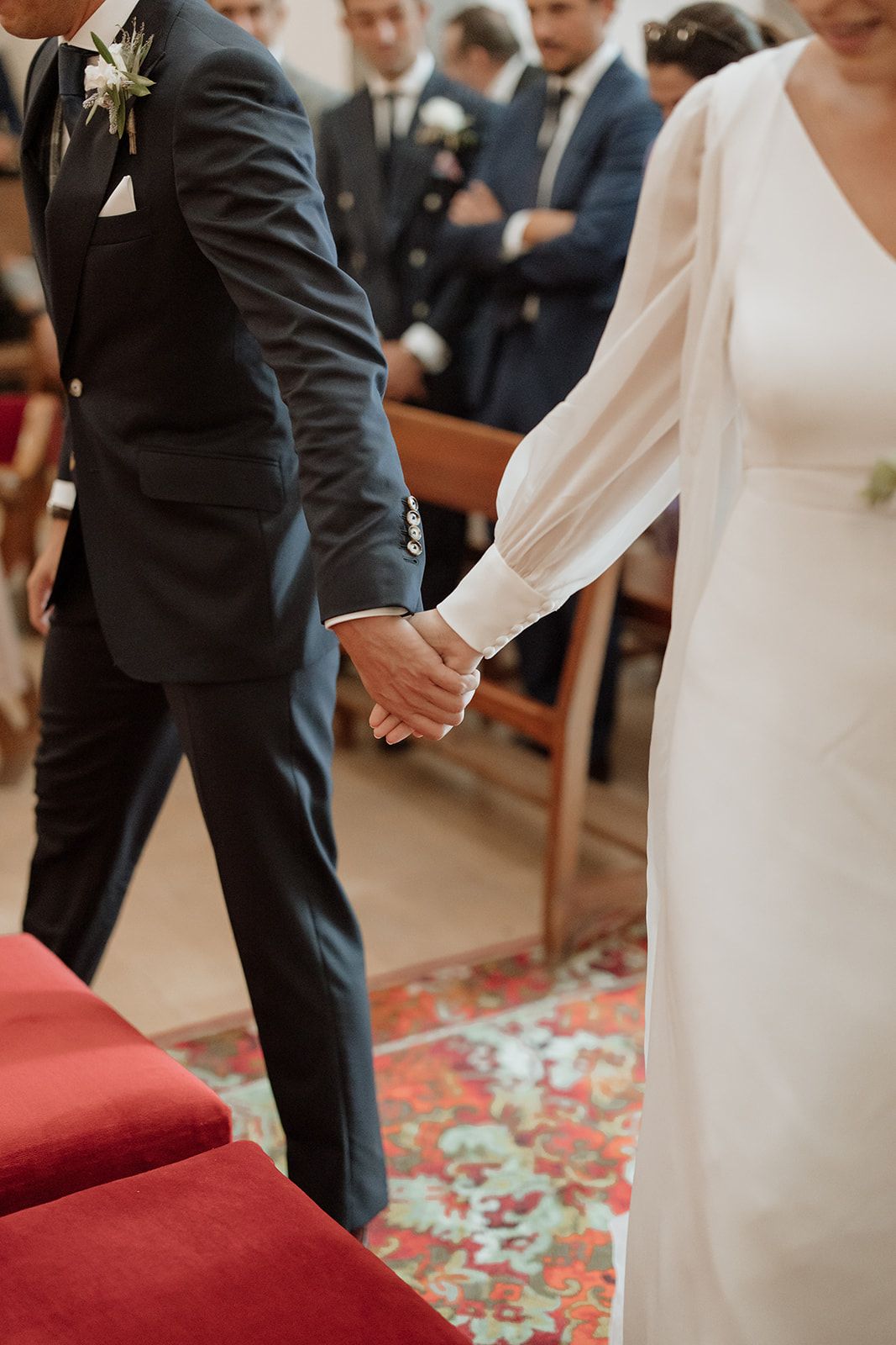 Close-up of bride and groom holding hands during wedding ceremony on decorative red carpet.