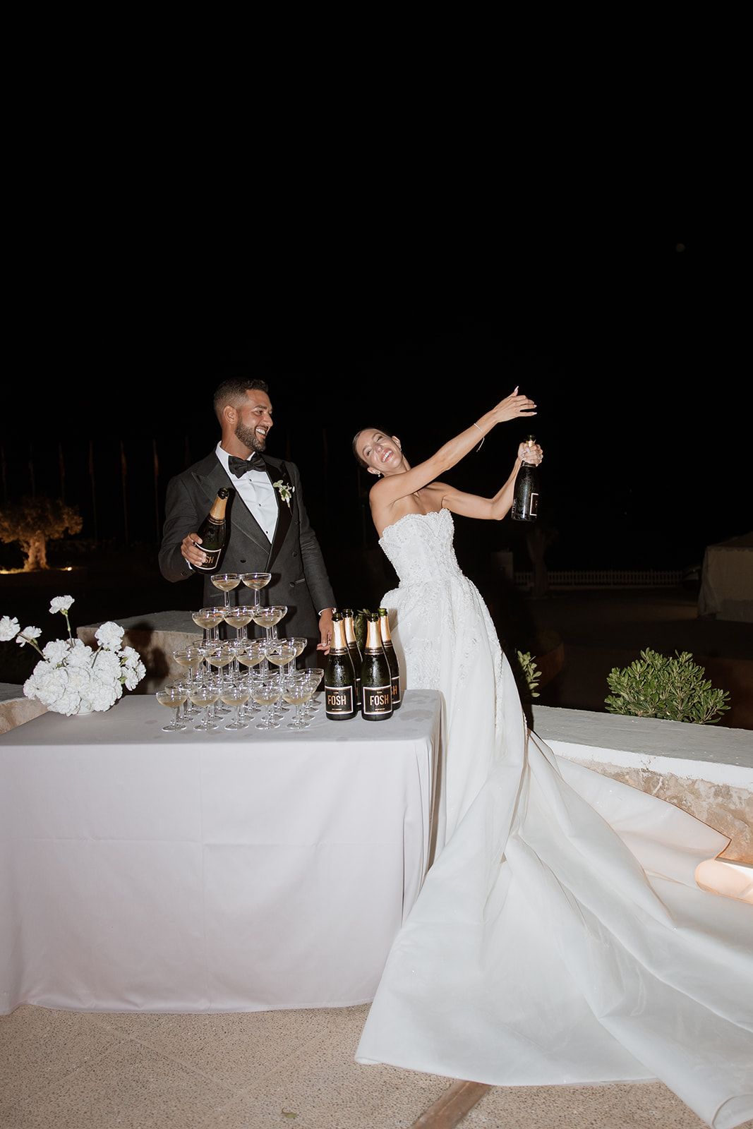 A couple celebrates at their wedding champagne tower during an evening reception.