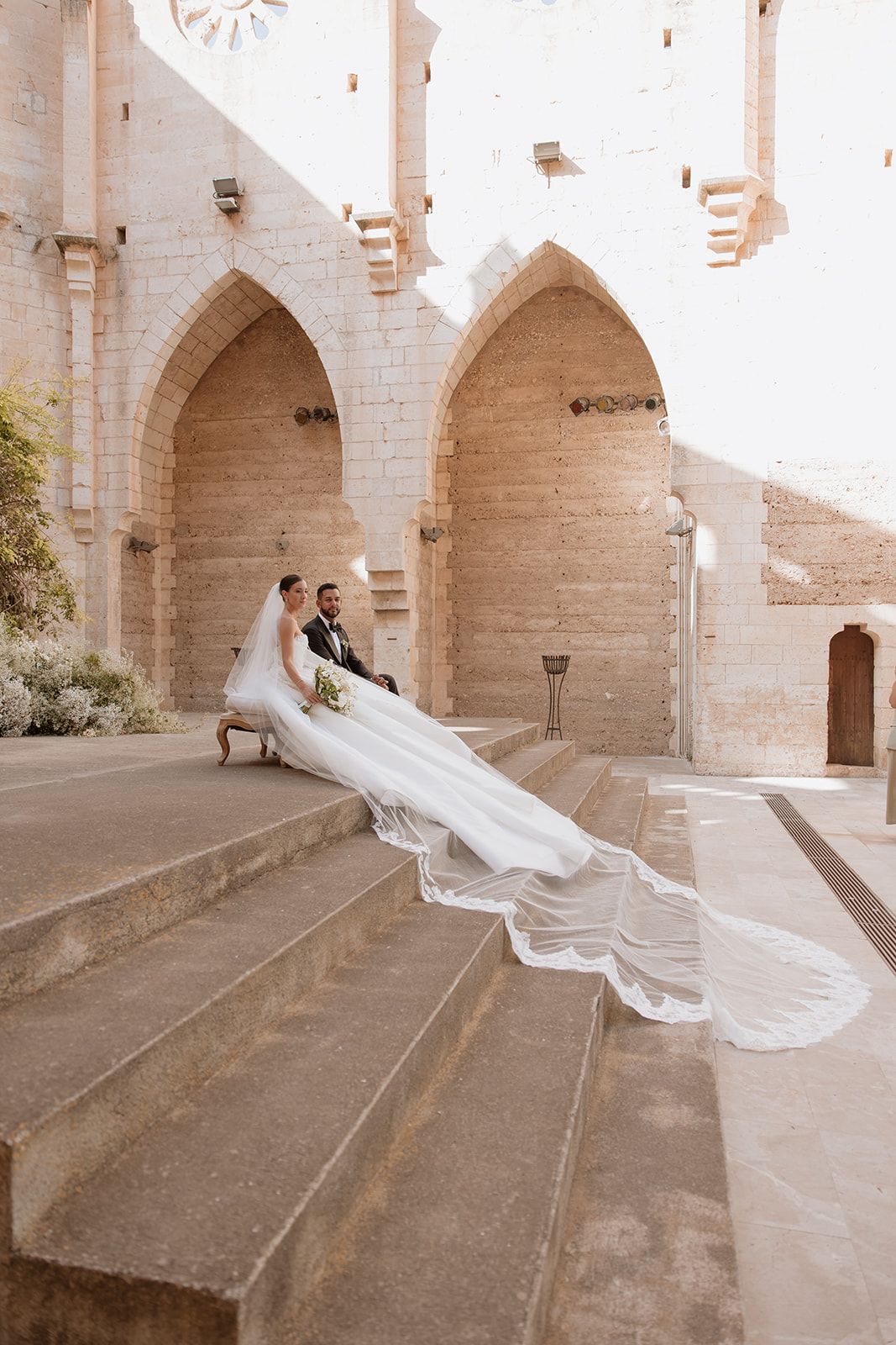 A dramatic wedding photo captures a flowing veil cascading down stone steps at a historic venue.