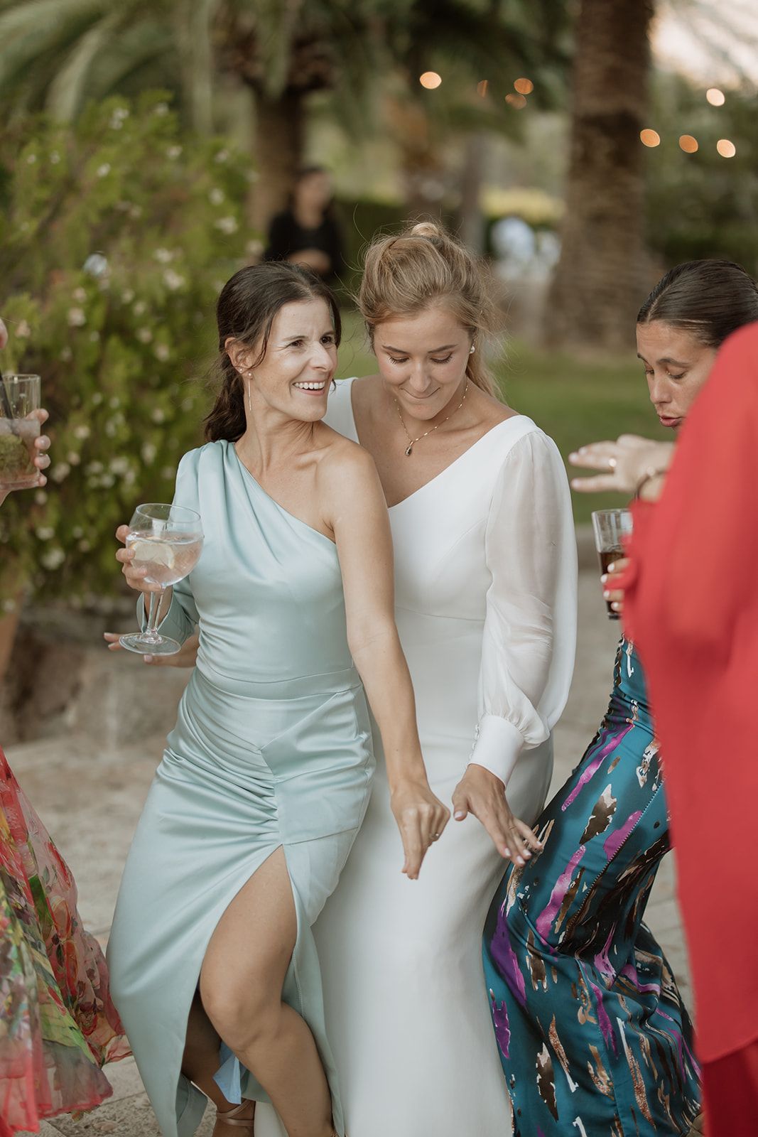 Guests in elegant dresses enjoying a festive outdoor wedding reception with string lights.
