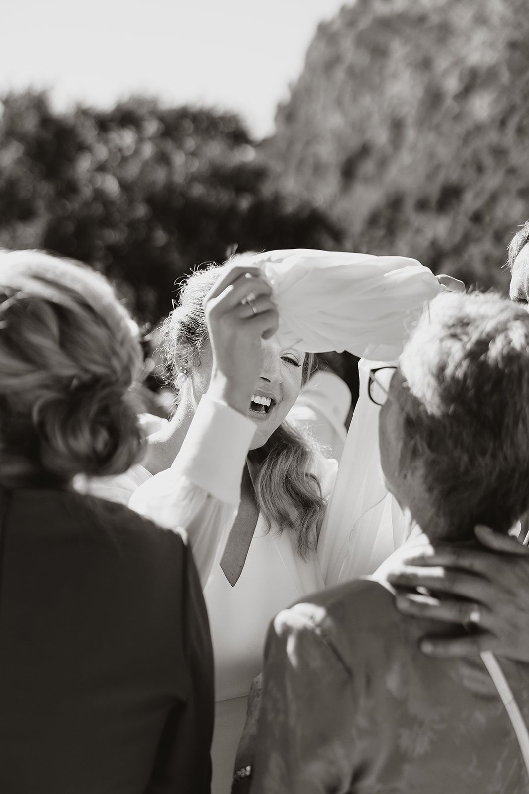 A black and white photo captures candid laughter during an outdoor wedding celebration.