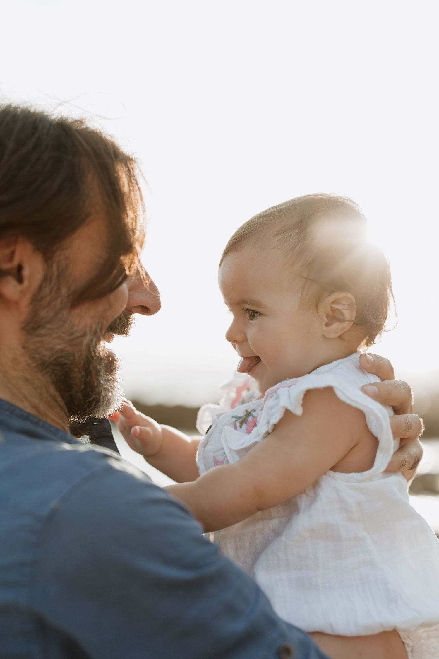 A heartwarming interaction between a bearded adult and a smiling baby in white clothing.