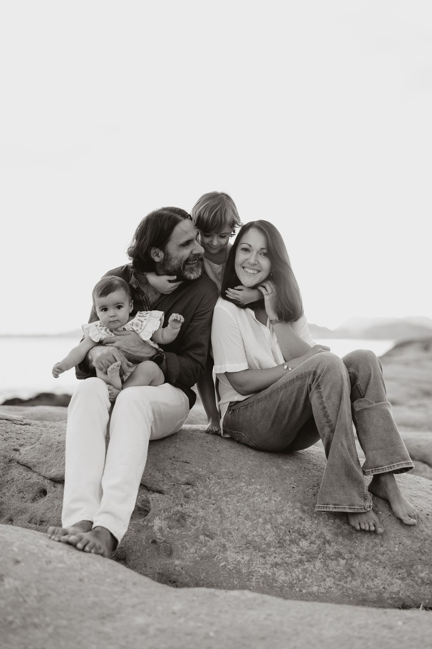 A black and white portrait of a family sharing affectionate moments on rocky terrain.