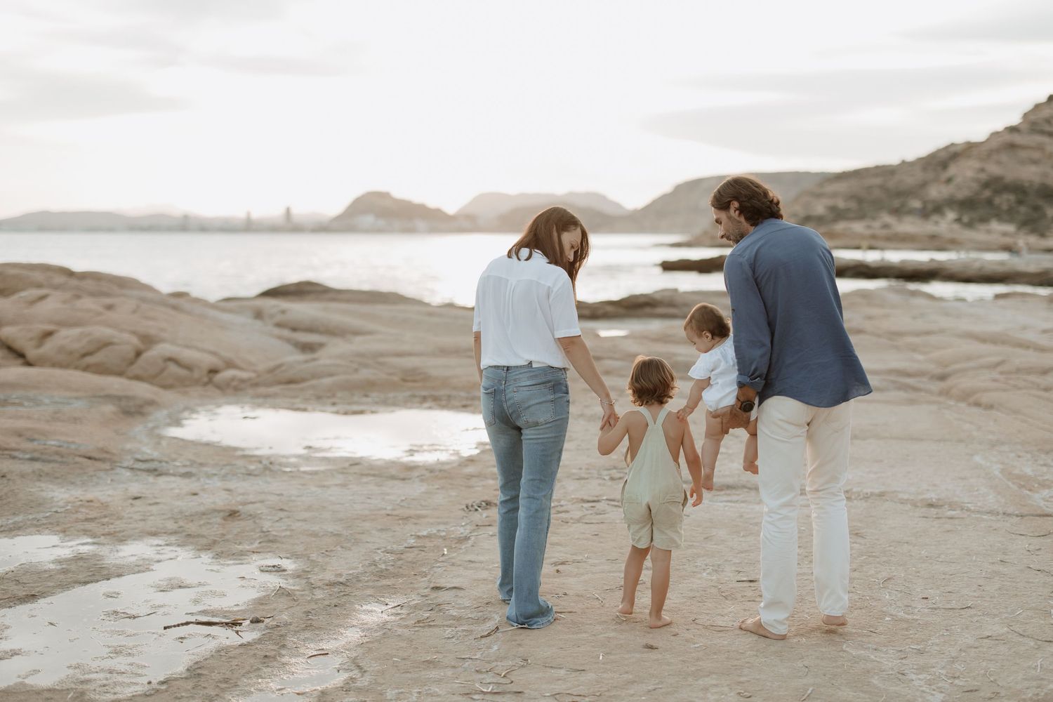 Family explores rocky coastal landscape together during sunset.
