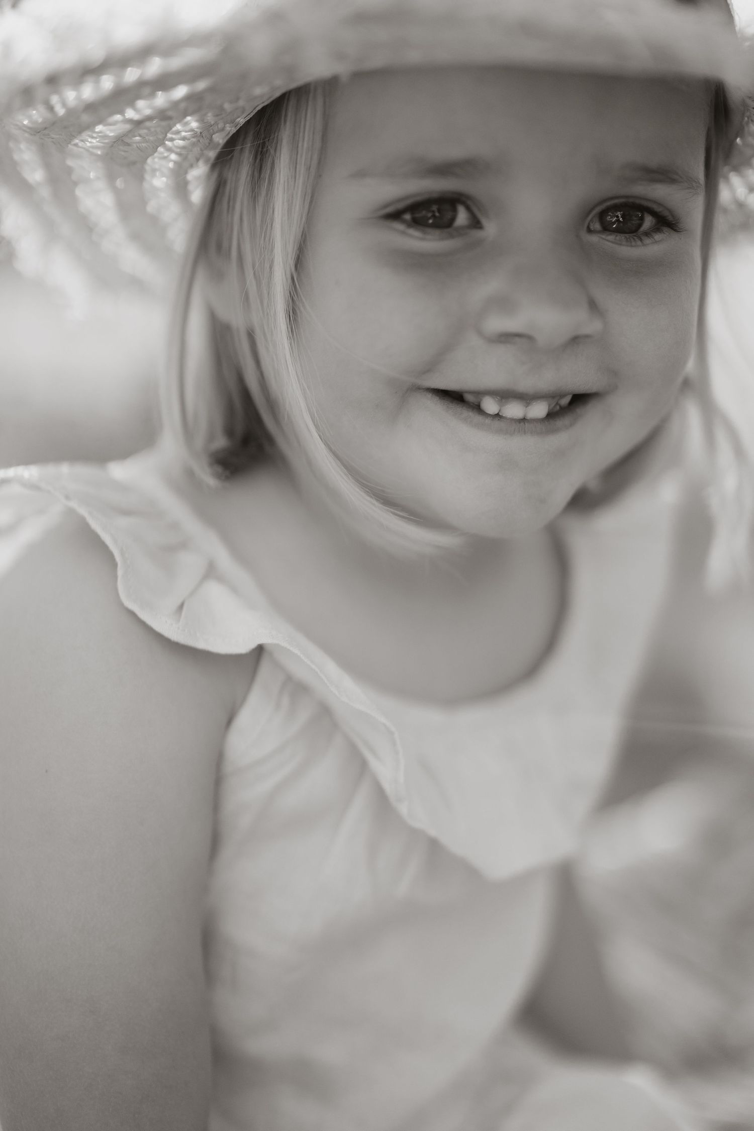 Black and white portrait of young child wearing white ruffled top and smiling at camera.
