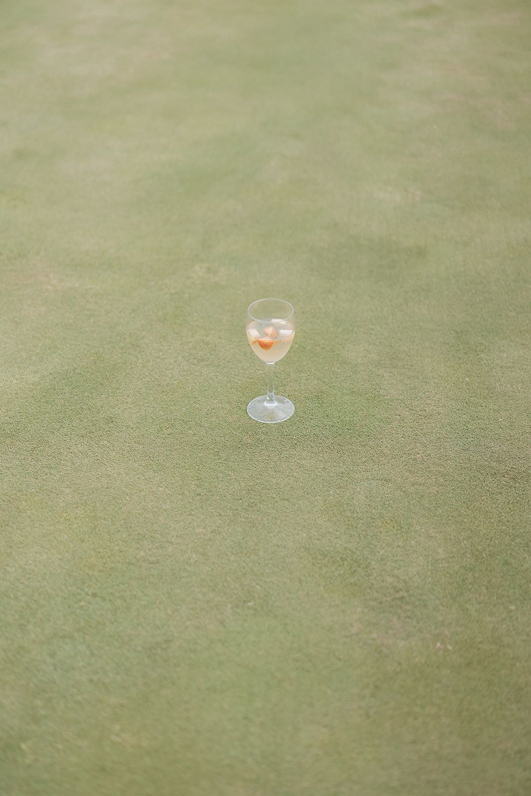 Wine glasses sitting on a green grass lawn during an outdoor wedding reception.