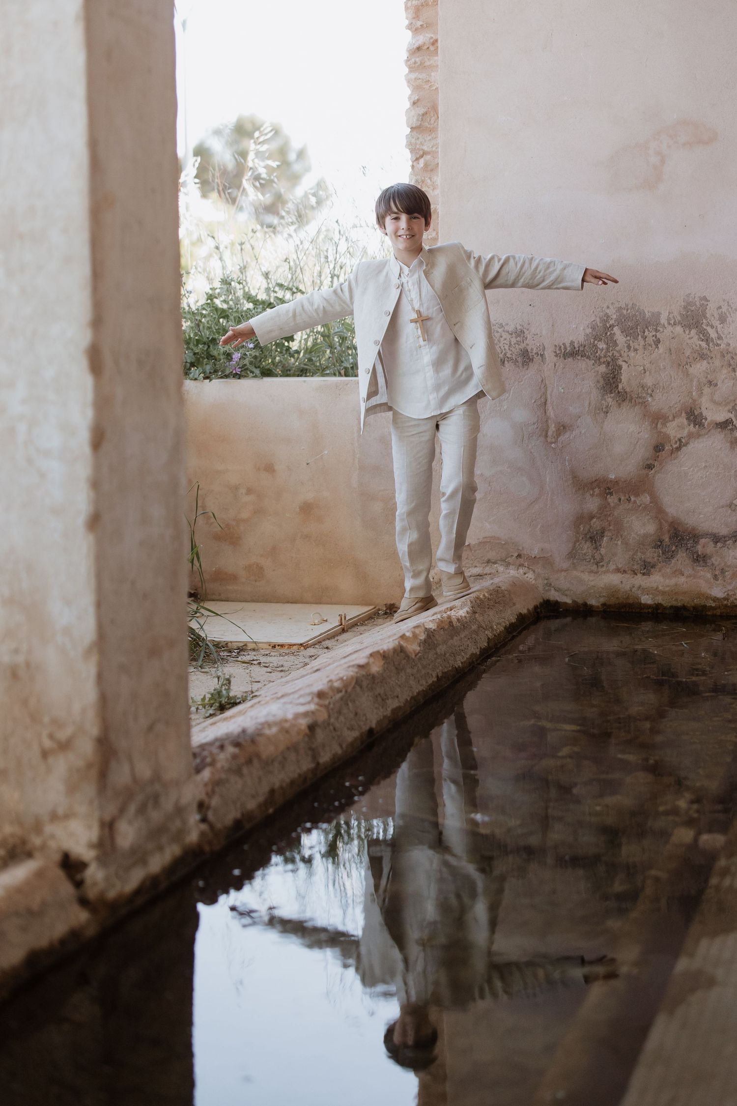 Four sequential images showing a person's reflection in still water against a weathered architectural backdrop.