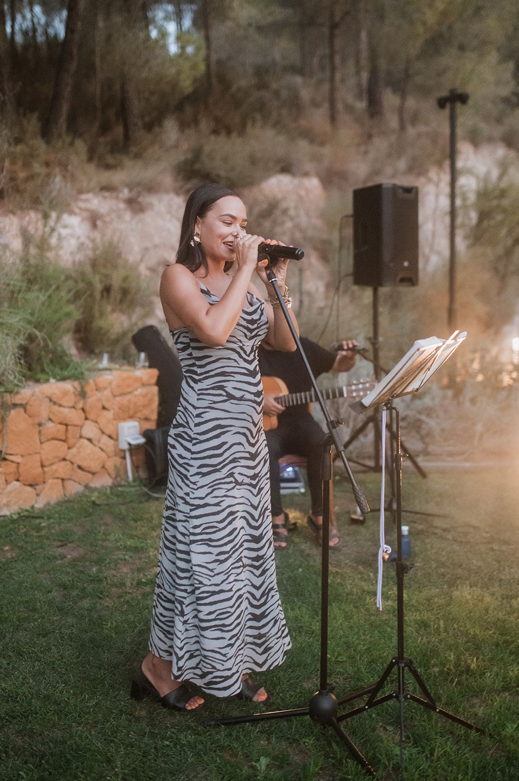 Singer in zebra print dress performs at outdoor wedding reception with guitar accompaniment.