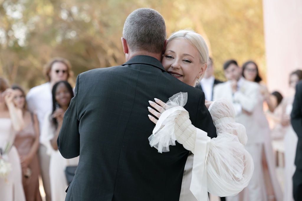 An emotional embrace during a wedding dance with guests looking on in background.