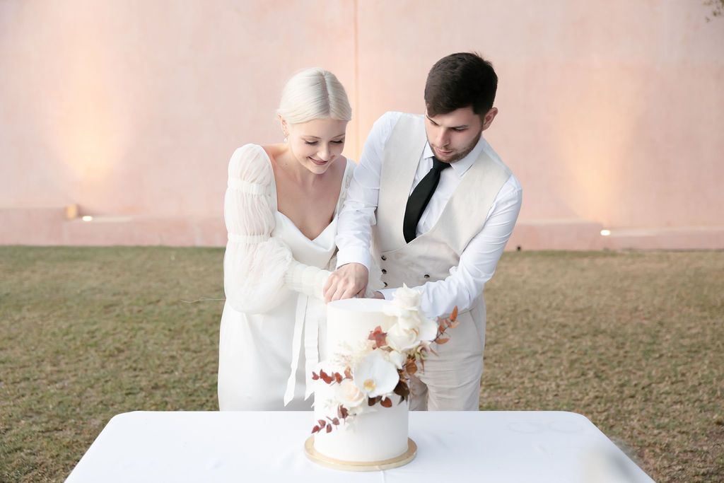 Wedding couple cutting their elegant white cake decorated with floral accents.