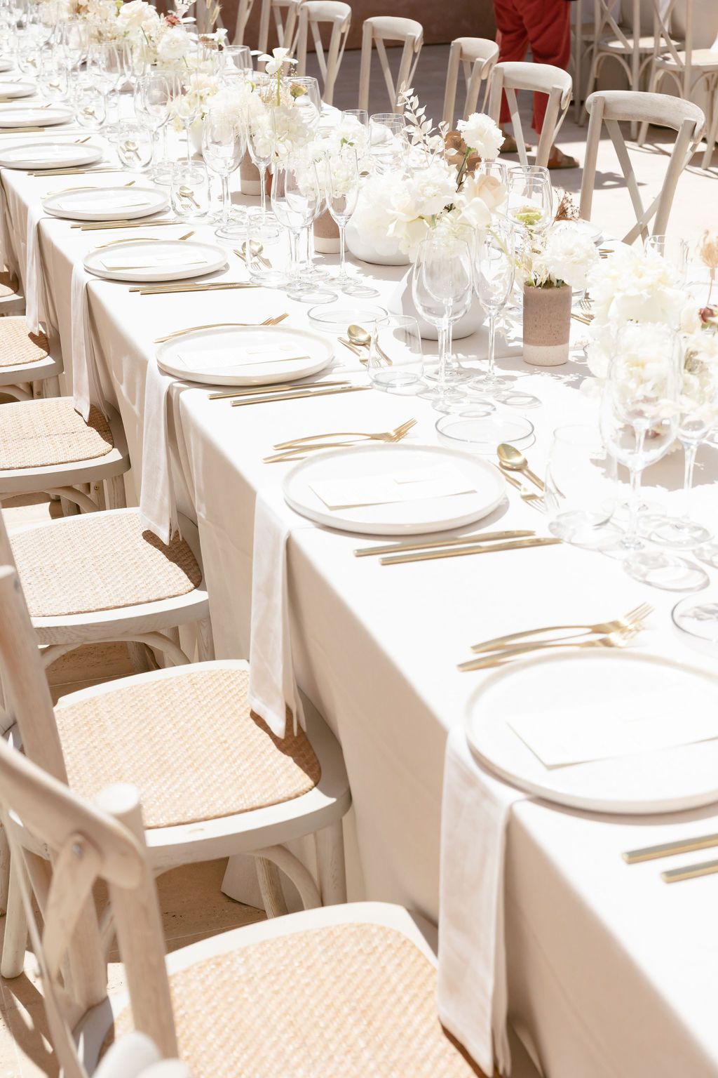 Elegant wedding reception table setup with white linens and crossback chairs in natural light.