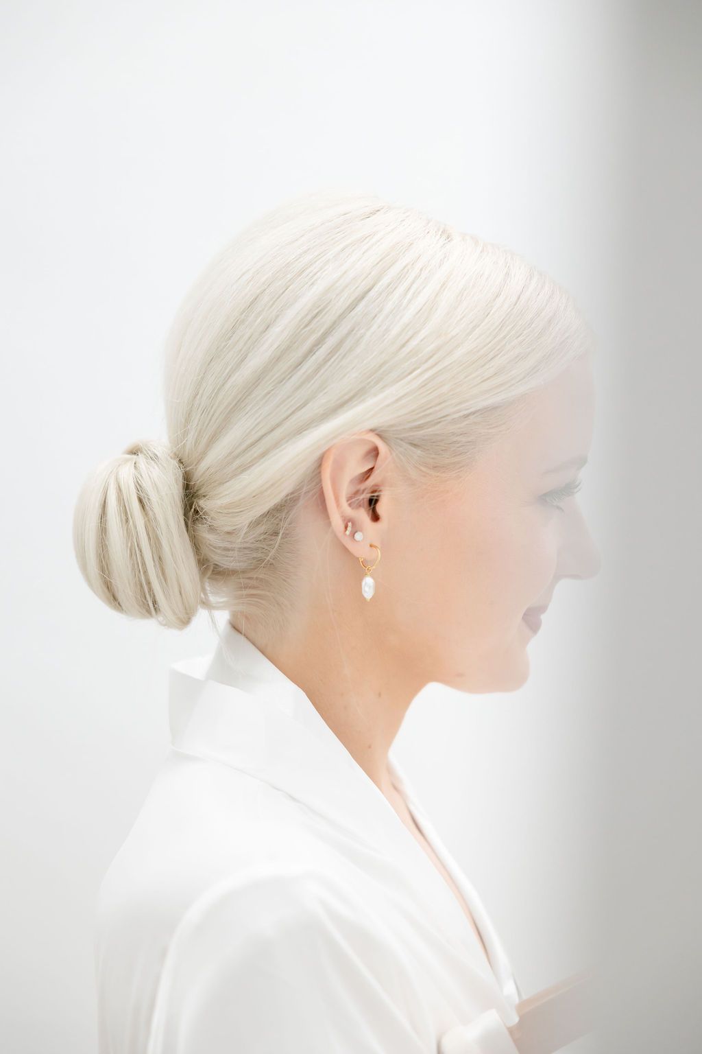 Side profile showing elegant pearl drop earring and sleek updo hairstyle.