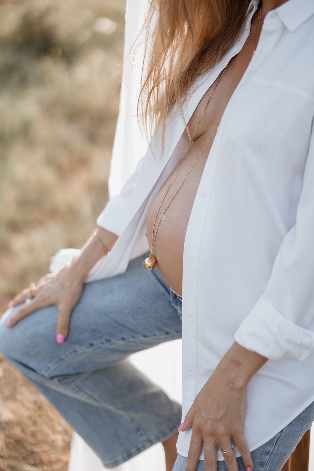 Close-up detail shot of white shirt and denim during outdoor maternity session.