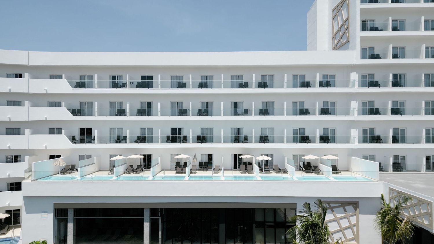 Modern white beachfront hotel featuring a distinctive architectural design with rows of balconies and a rooftop pool.
