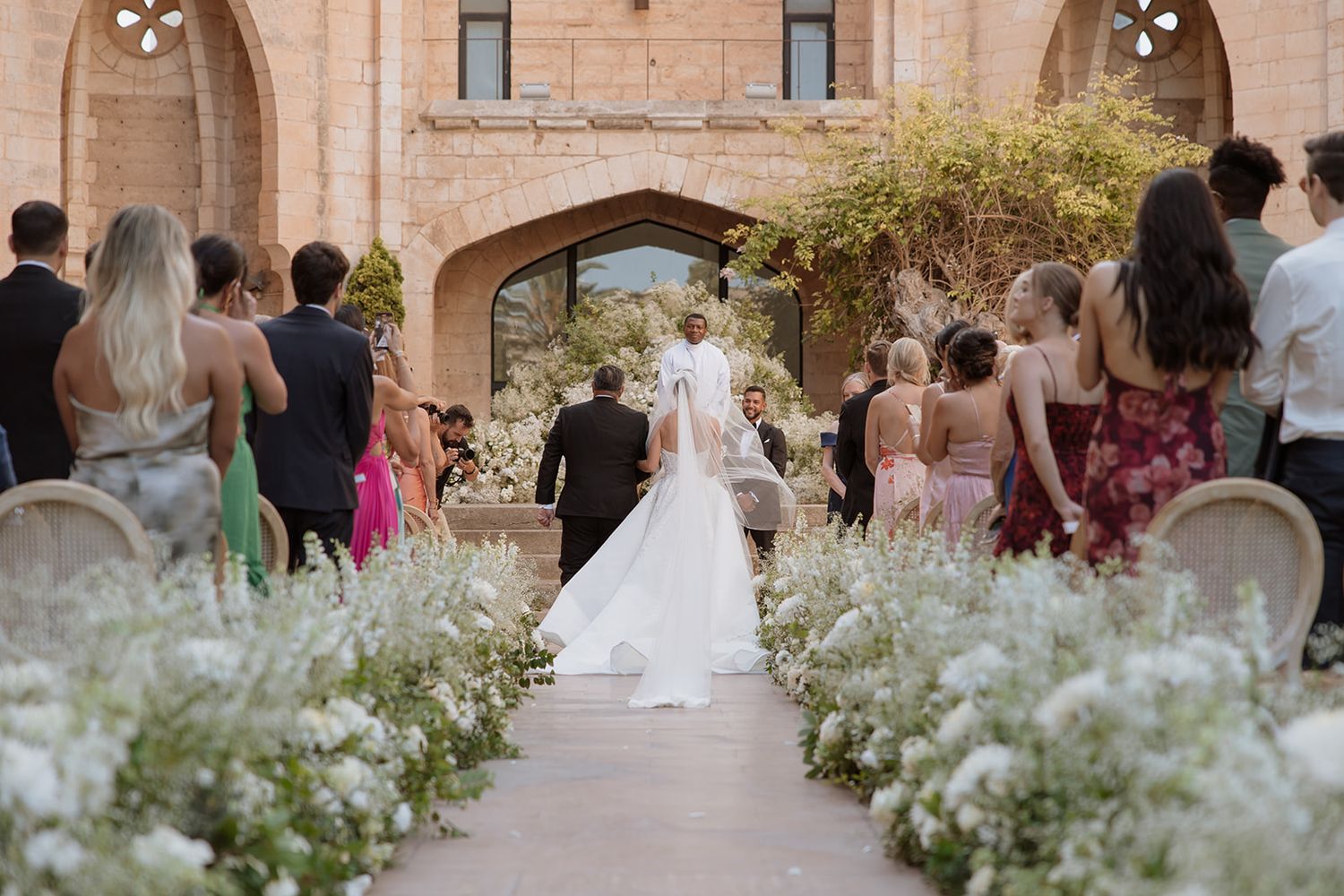 Wedding guests line a floral-decorated aisle as a couple celebrates their ceremony at a historic venue.