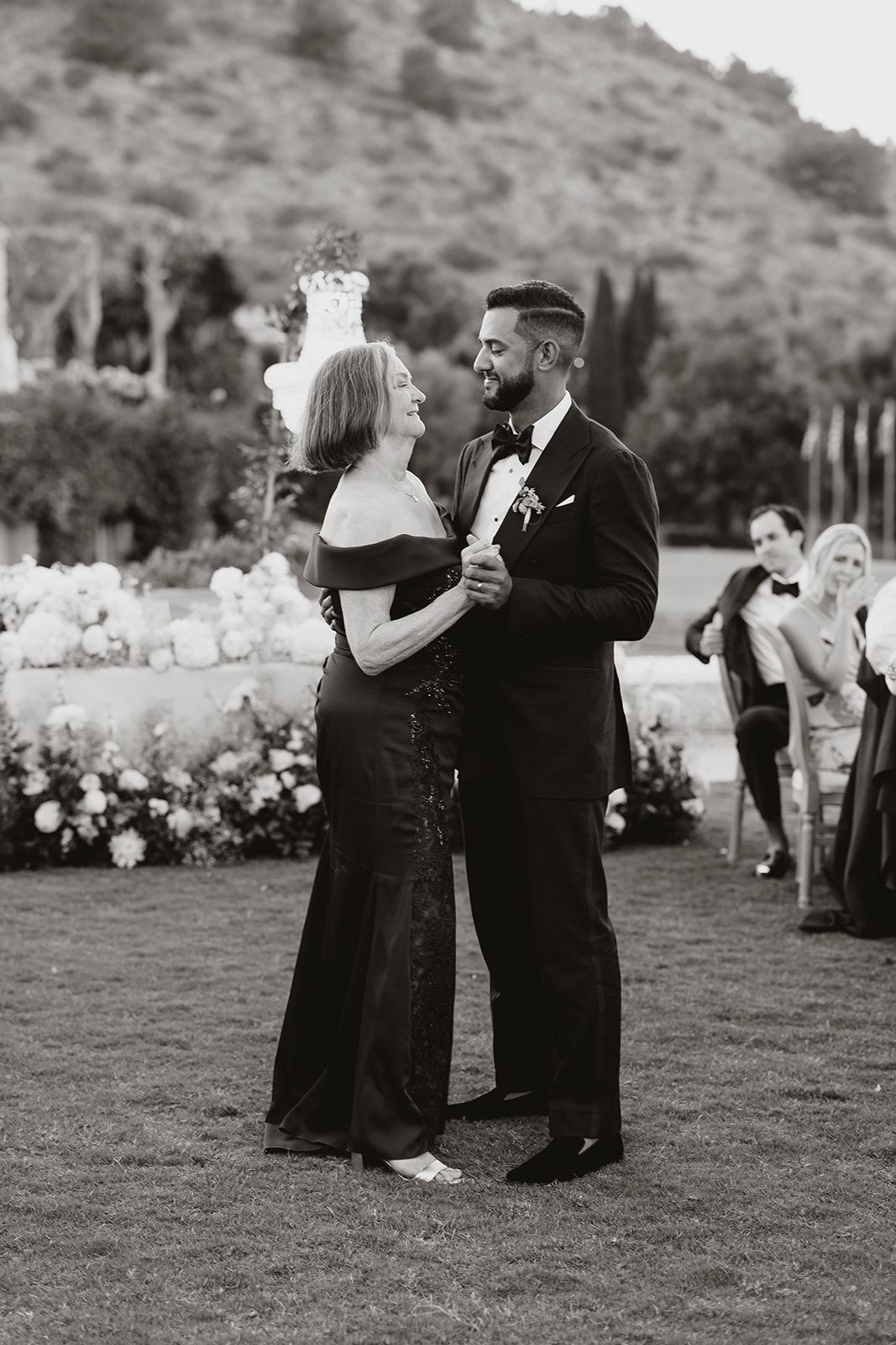 A couple shares a dance during an evening wedding reception on a garden lawn.