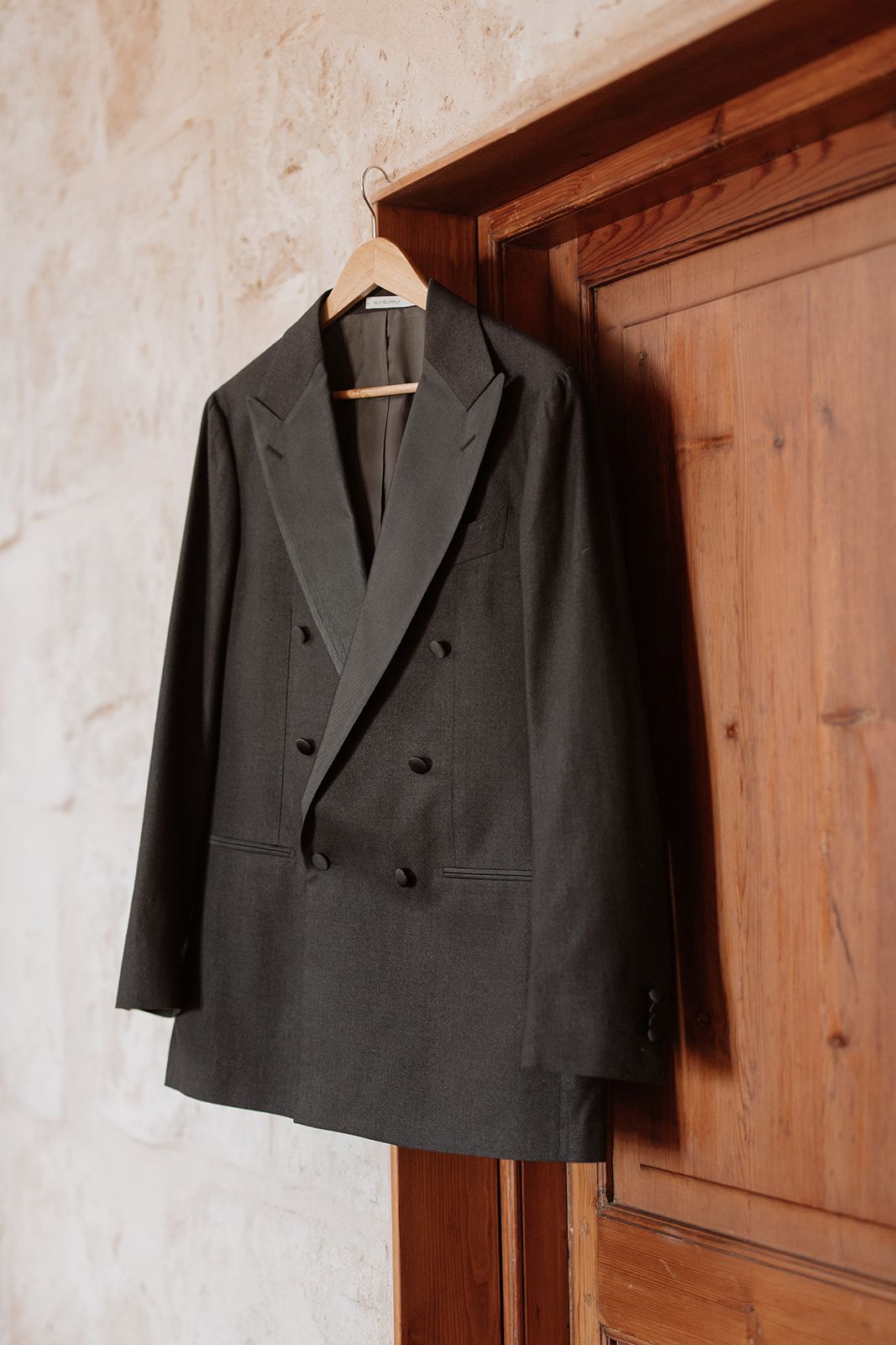 Dark formal suit jacket hanging on wooden wardrobe in natural light.