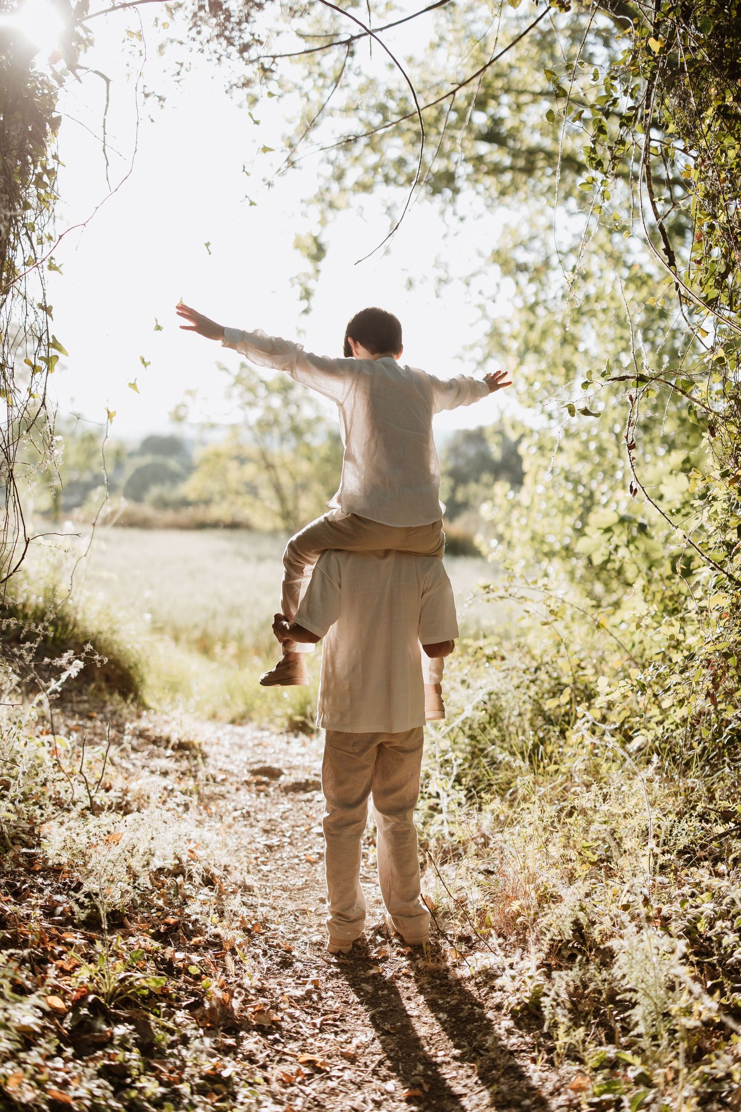 Two people enjoying a joyful moment on a sunlit nature trail with arms spread wide in celebration.