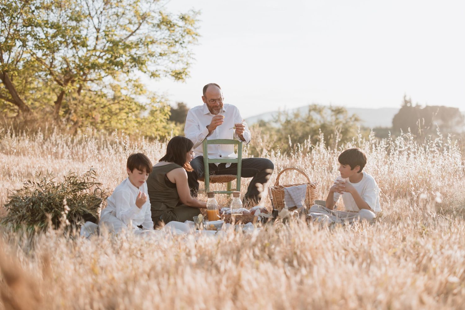 A group enjoys a casual outdoor gathering in a golden field at sunset with rustic table settings.