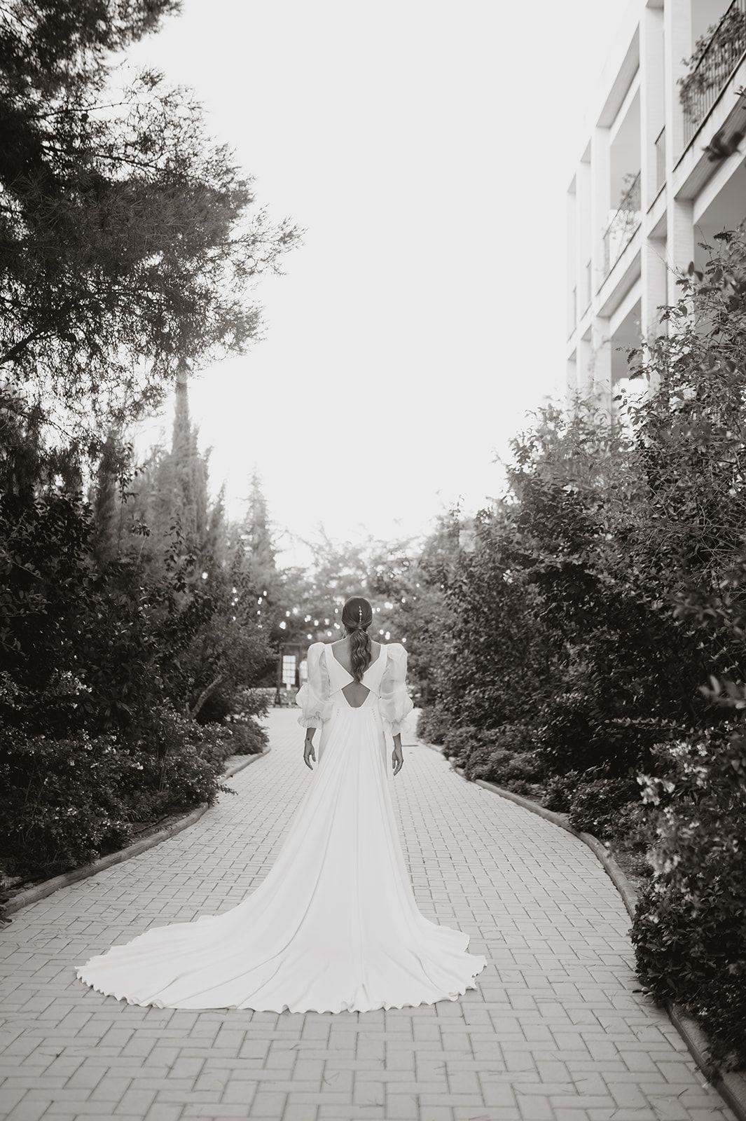 Black and white wide shot of couple on brick pathway with trailing wedding dress.