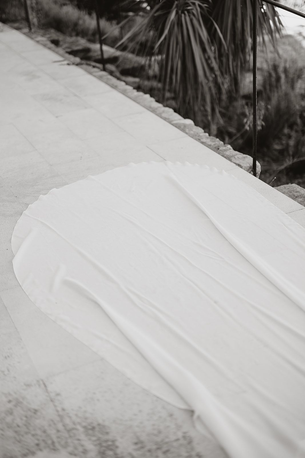 Black and white detail shot of wedding dress train on stone patio.
