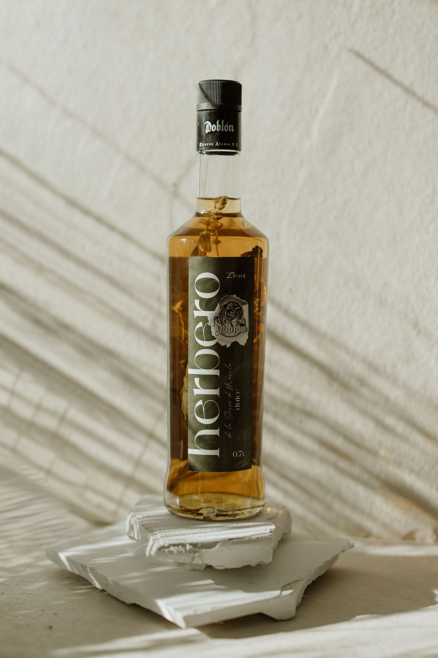 A bottle of Herbero spirits balanced on stacked white coasters against a light background.