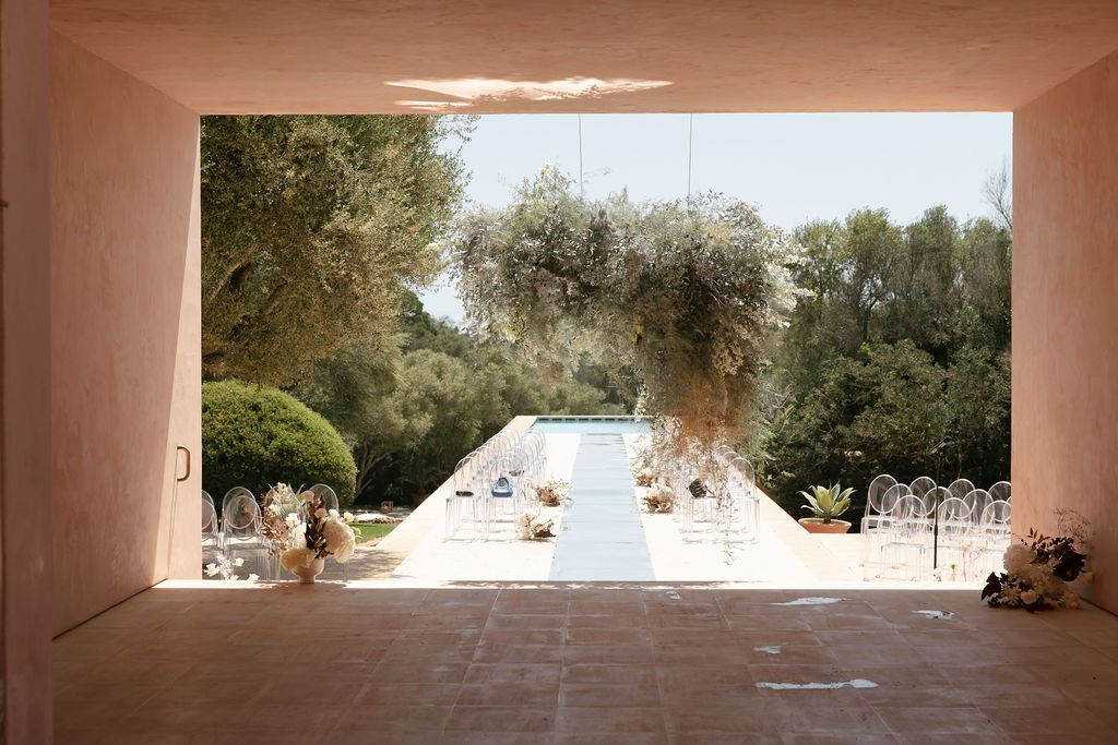 Framed view through an archway of an outdoor wedding ceremony setup with white chairs.