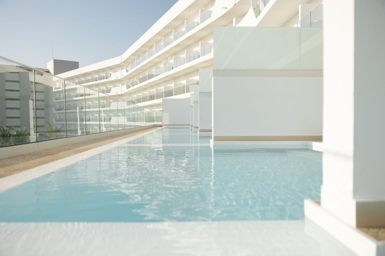 Modern outdoor swimming pool surrounded by sleek white building architecture and balconies.