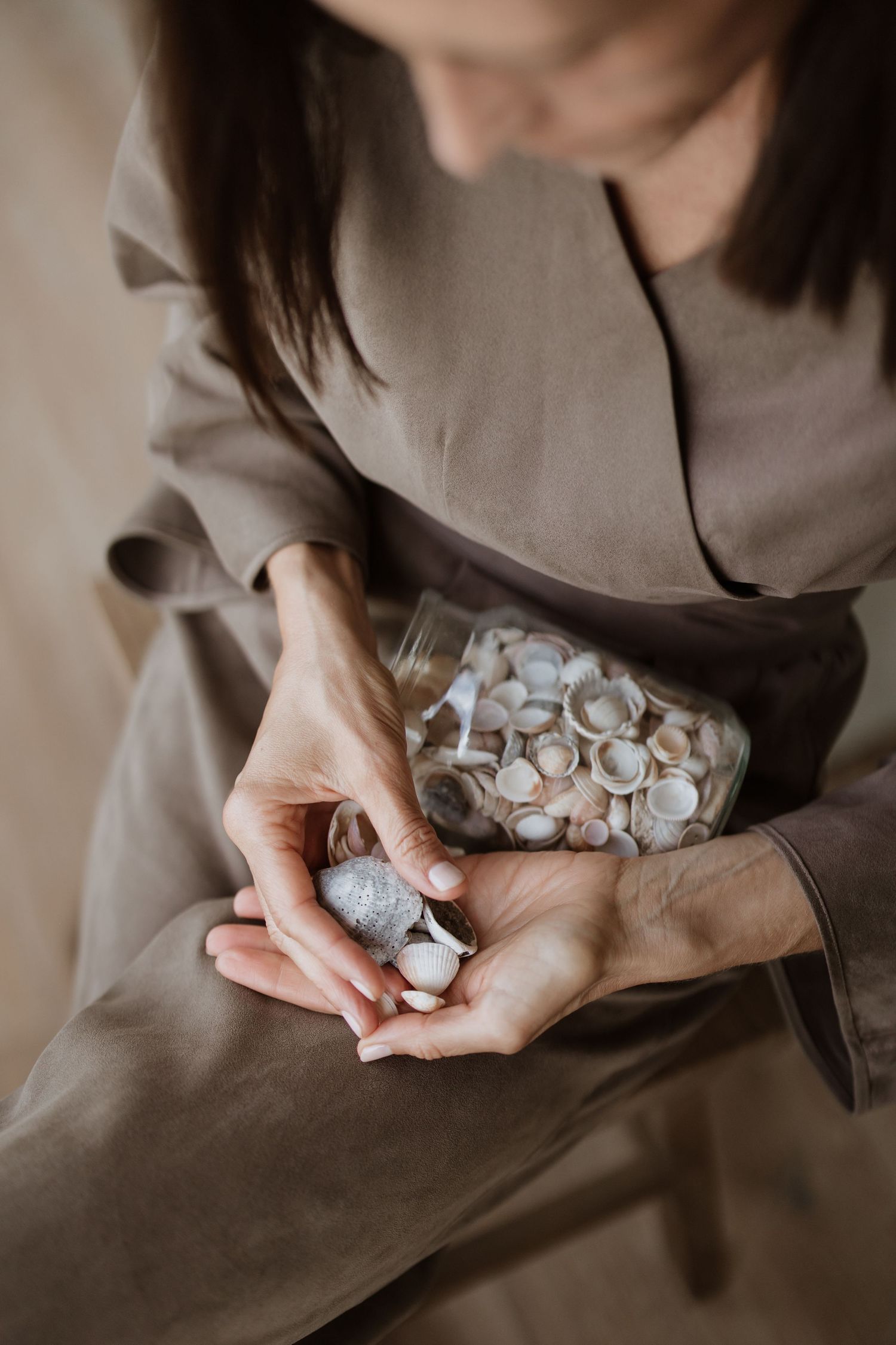 Hands holding a glass jar filled with small white seashells against a neutral dress.