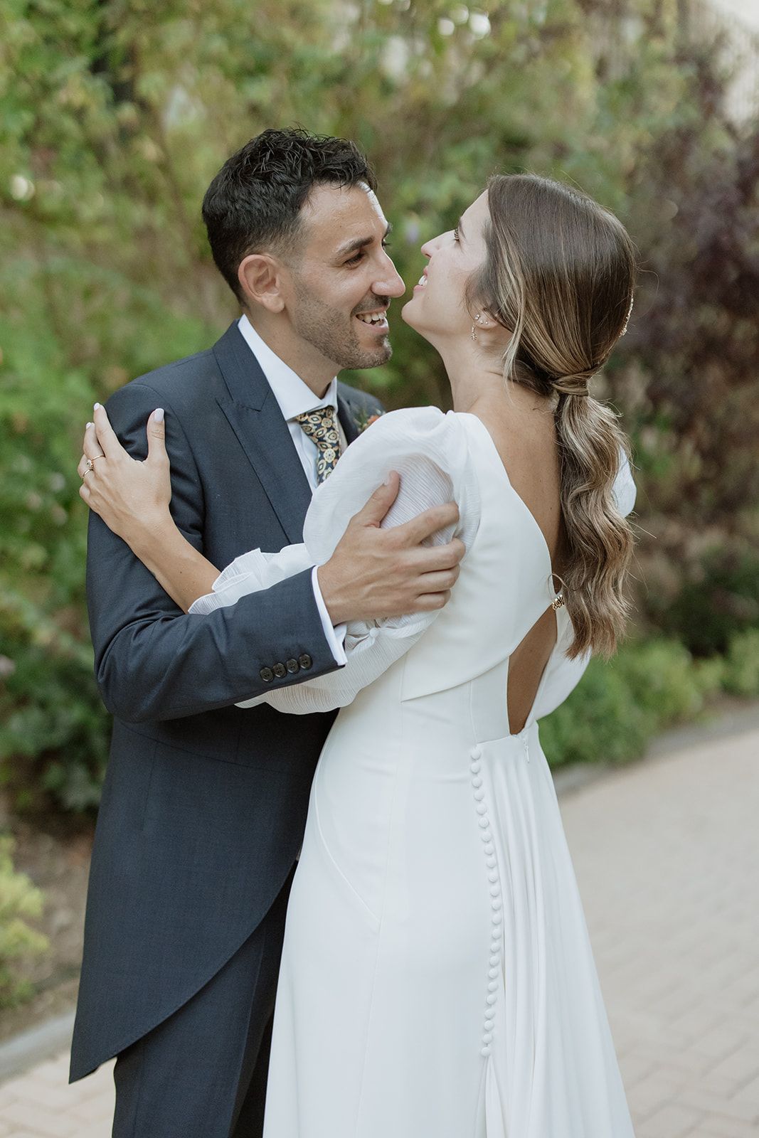 Wedding couple shares joyful moment on brick pathway surrounded by garden foliage.