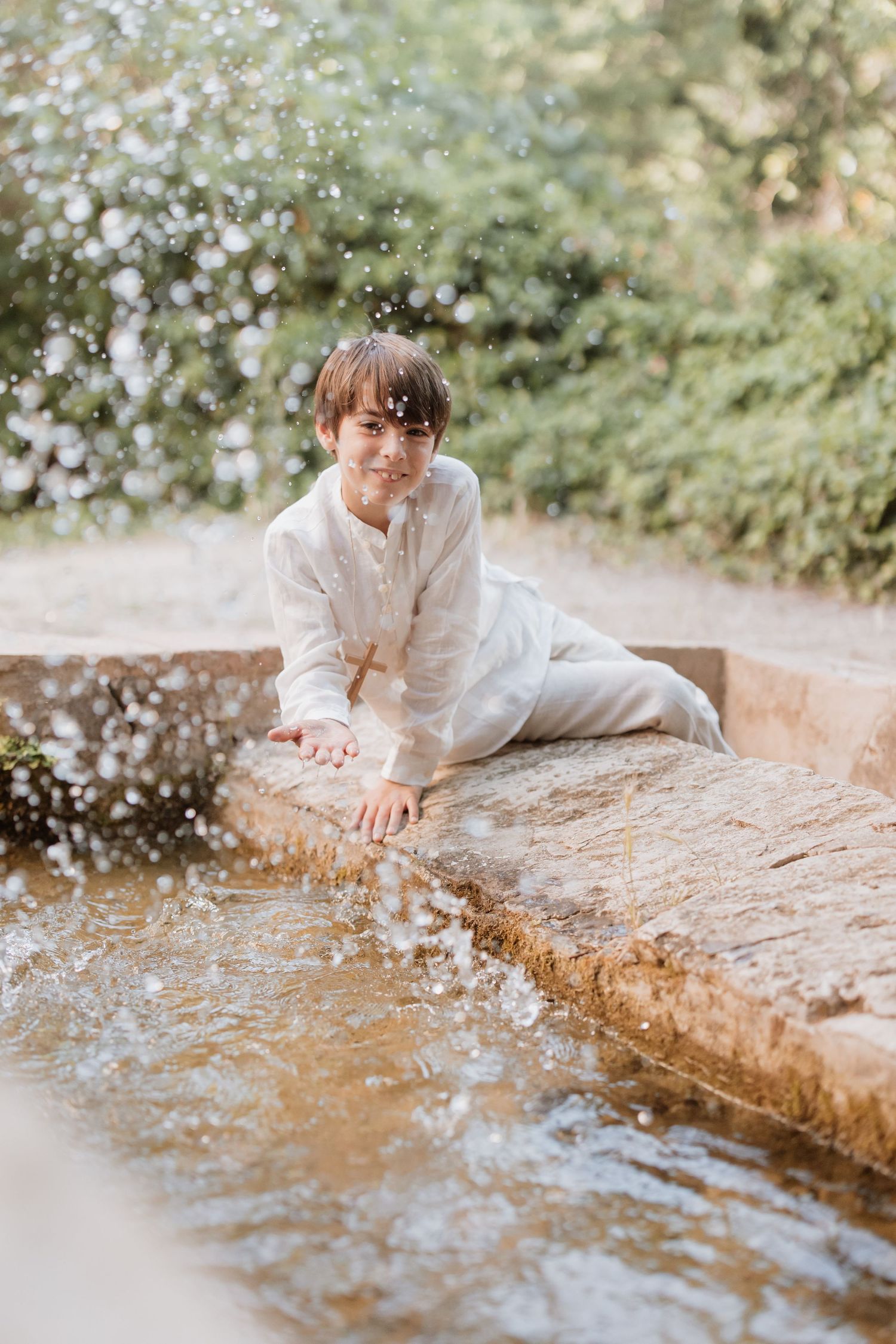 A white-clothed figure poses playfully by a flowing stream in a dreamy outdoor setting with bokeh effects in the background.